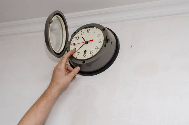 Old Navy Submarine Wall Clock. A man's hand corrects the minute hand on a Mechanical Clock. Indoors. Selective focus.
