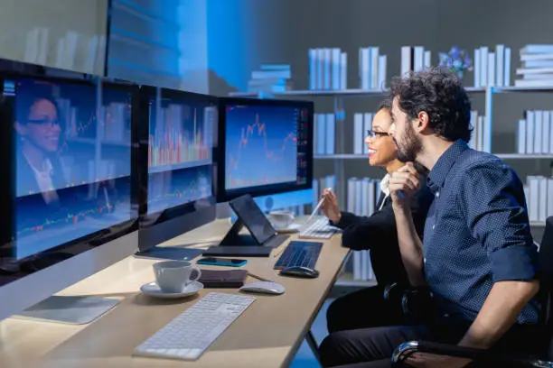 team brokers look at stock market graph on monitor computer to analyze before offer and arranges transactions between buyer and seller for a commission when the deal is executed