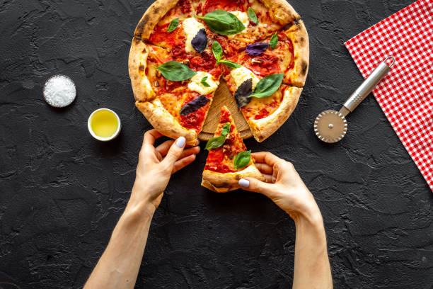 istock Female hands hold slice of pizza. Overhead view 1352485615