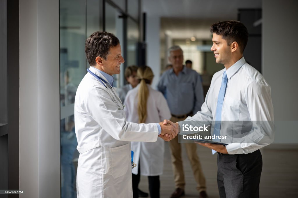 Medical sales representative greeting a doctor with a handshake at the hospital Latin American medical sales representative greeting a doctor with a handshake at the hospital while presenting some medicines - pharmaceutical industry concepts Doctor Stock Photo