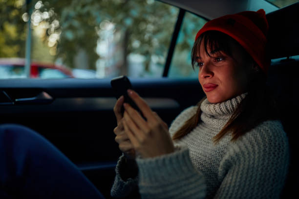 istock Young woman sitting on backseat in car and using phone 1352493469