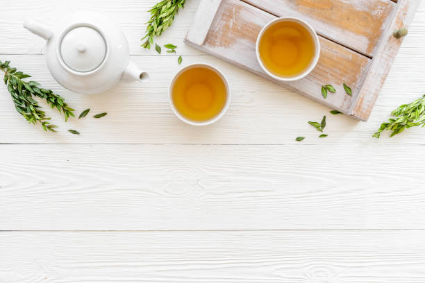 istock Tea drinking with white teapot and two cups with green leaves, top view 1352493593