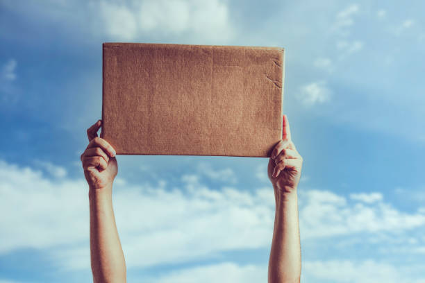 istock Man holding blank piece of cardboard against blue sky 1352493683