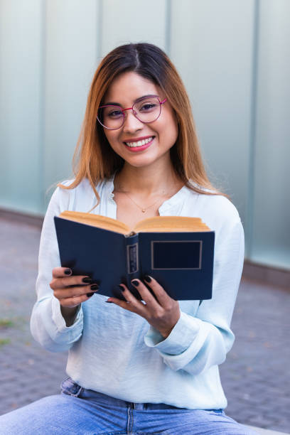 istock Positive optimistic brunette woman with glasses smiling while sitting outdoors reading book. Copy space for text 1352494160
