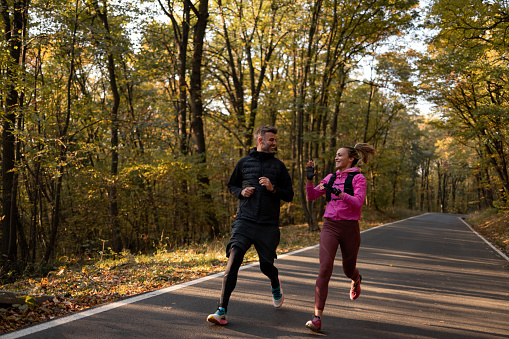Man and woman running in the forest road and having a good time during training