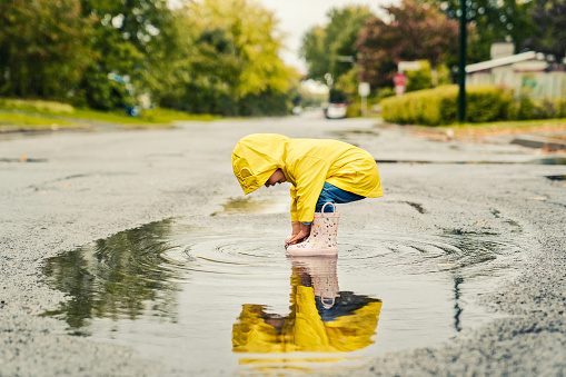 Divertida y linda niña con abrigo amarillo impermeable y botas jugando bajo la lluvia photo