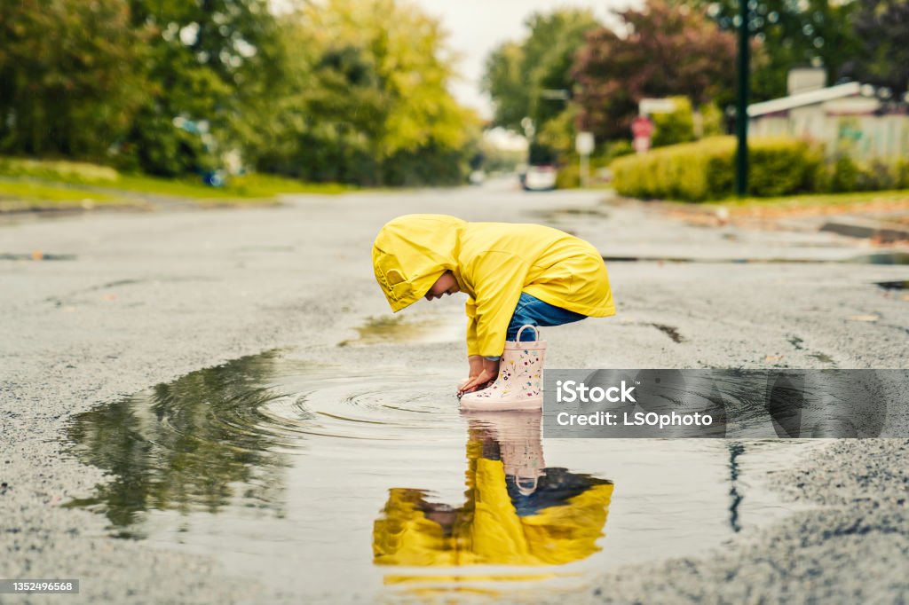 Funny cute baby girl wearing yellow waterproof coat and boots playing in the rain A Funny cute baby girl wearing yellow waterproof coat and boots playing in the rain Child Stock Photo
