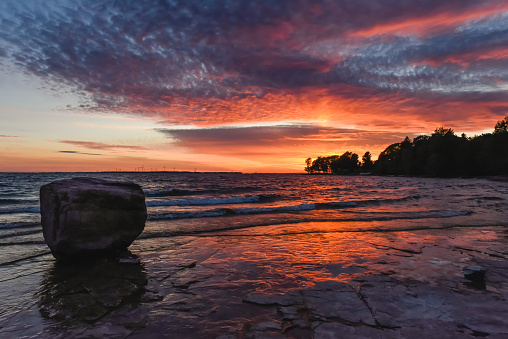 Beautiful colorful sunset on shoreline of lake with large rock. in Kingston, Ontario, Canada