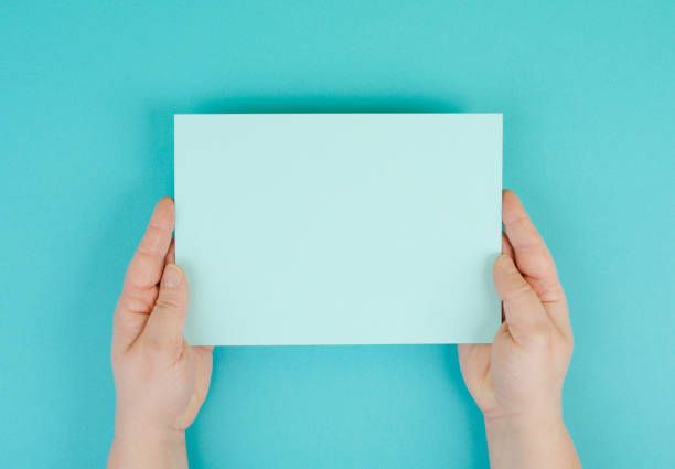 istock Woman holds a blank sheet of paper, blue colored background, empty copy space for text, minimalism 1352496934