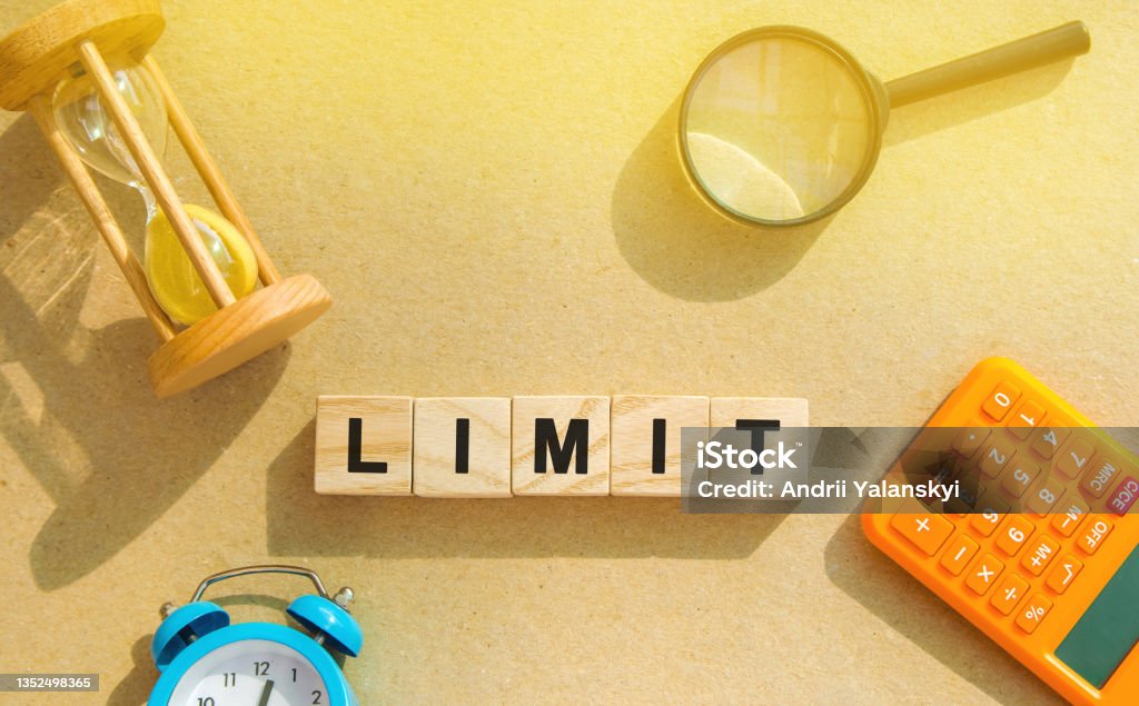 Wooden blocks with the word Limit, hourglass, magnifying glass. Risk management in the banking and financial sector. Business and finance concept. Quantitative limitation, maximum range. At The Edge Of Stock Photo