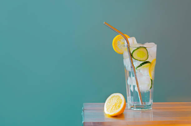 istock Refreshing tonic and gin Tom Collins cocktail or lemonade with lemon ice and cucumber on contrast colorful blue and yellow background. Bar menu, alcohol recipe decor, specialized website blog design 1352498499