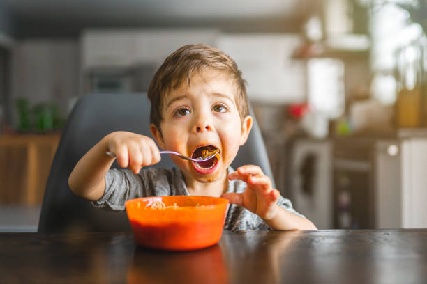 enfant mangeant des spaghettis dans la cuisine - child eating pasta spaghetti photos et images de collection