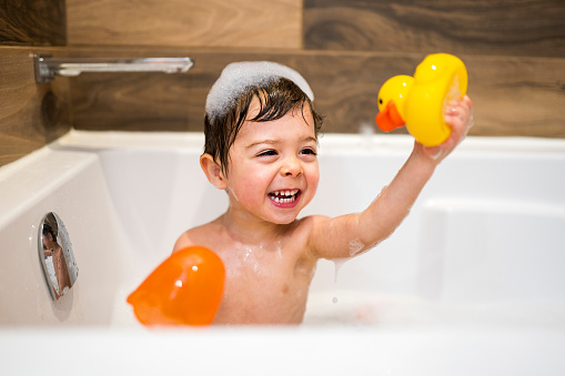 Happy two-year kid bathes with toys in bath