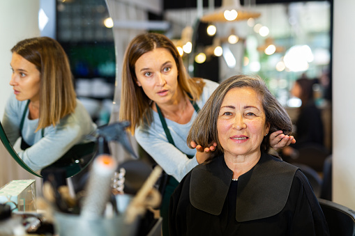 Professional hair stylist discussing elderly female customer preferences in salon, choosing new hairdo