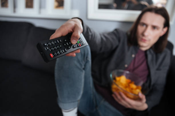istock Young man sitting at home indoors. Focus on remote control. 1352501305