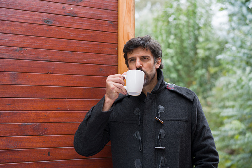 Portrait of a  man wearing a coat and having coffee outside a wilderness resort cabin