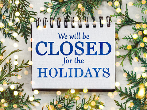 Signboard with the inscription We will be closed for the holidays and green branches of a Christmas tree. View from above, closeup, indoors, no people. Congratulations for family, friends, colleagues