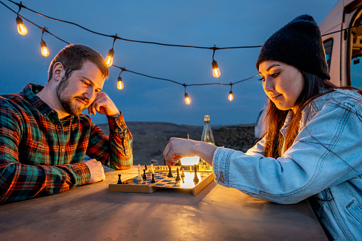 Young Couple Out Camping Playing Chess Together At A Picnic Table