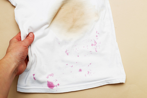 dirty stains on a white T-shirt from berries and drink on brown background.