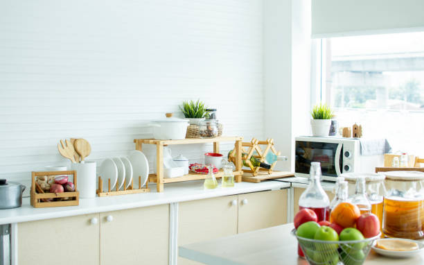 istock Interior design background with nobody of white clean kitchen room with window and day light in cozy home. There are wooden kitchenware and vegetables on table counter bar. 1352510508