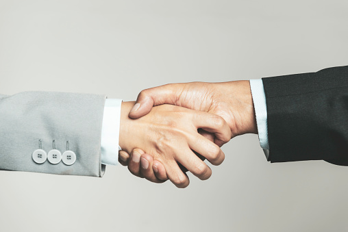 Handshake on light grey background, copy space. Businessmen wear smart suits. Business and agreement concept. Male hands shaking tight in a deal, close up.