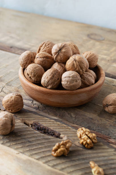 les noix sèches se trouvent dans un bol en bois et plusieurs noix sont hachées sur une table en bois. style rustique. concept de nutrition saine. orientation verticale. - dried fruit variation healthy eating snack photos et images de collection