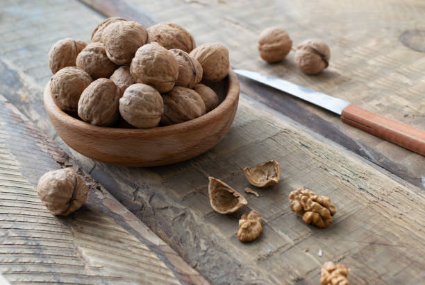 les noix sèches se trouvent dans un bol en bois et plusieurs noix sont hachées sur une table en bois. style rustique. concept de nutrition saine. - dried fruit variation healthy eating snack photos et images de collection