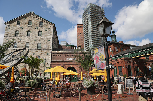 Toronto, Canada - September 5, 2021: The Distillery Historic District offers a pedestrian zone surrounded by industrial buildings housing retailers, restaurants and cultural venues. Visitors enjoy a weekend morning in one of Toronto's top attractions. Brick buildings stand near modern residential buildings in the southeast area of downtown.
