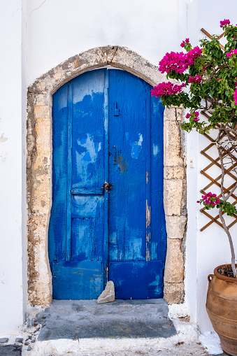 Greek island typical architecture. Kythira Chora town, Greece. Blue wooden door and red bougainvillea on whitewashed house wall. Sunny summer day