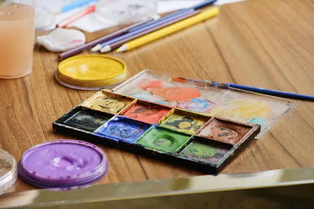 Artistic tools for drawing paintings on wooden table. Palette, watercolor, oil paints, brushes, colored pencils.