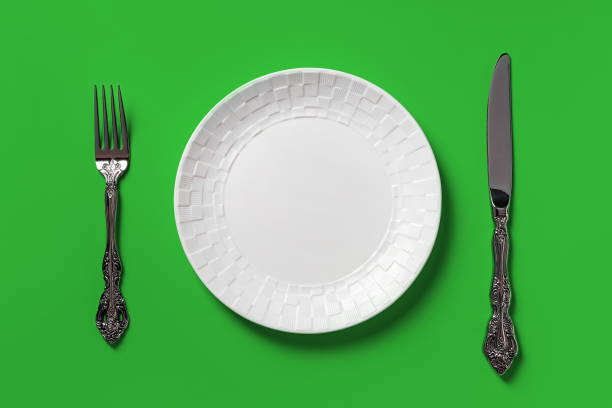 istock Empty white dinner plate, fork and table knife against green background. Blank mockup template for dieting, healthy eating and good eating habits concepts. 1352520043