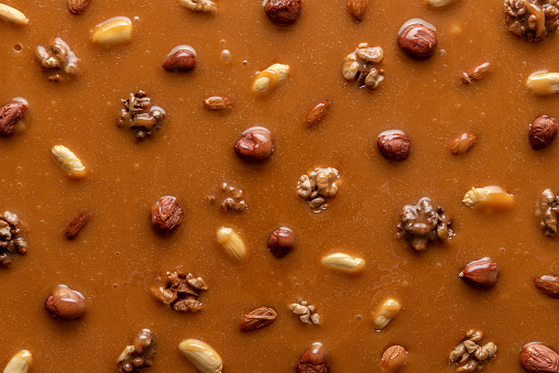 Melted caramel sauce with assorted nuts, full-frame image. Top view of peanut brittle ingredients. Caramelized hazelnuts and peanuts in caramel syrup