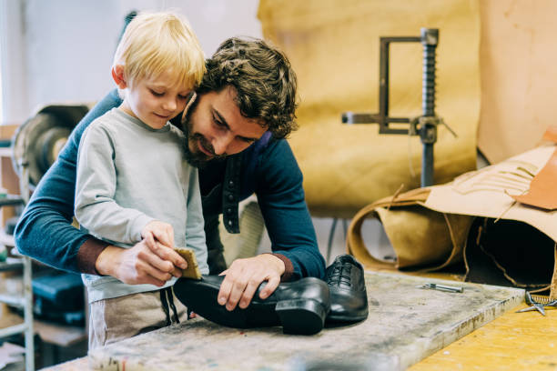 Shoemaker and his cute little boy in the workshop. Smiling father is teaching his son making a leather luxury shoes in the workshop. shoe mold stock pictures, royalty-free photos & images