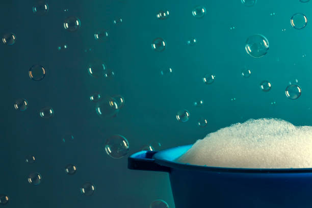 A DSLR photo of soap sud in a bowl with bubbles flying on a teal background.