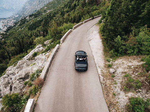 A man and a woman are driving in an open car along a scenic trail in the mountains in Montenegro . High quality photo