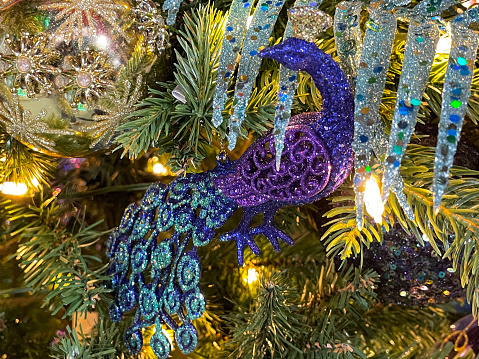 Stock photo showing a close-up view of artificial Christmas tree with peacock coloured themed glitter decorations and white fairy lights.