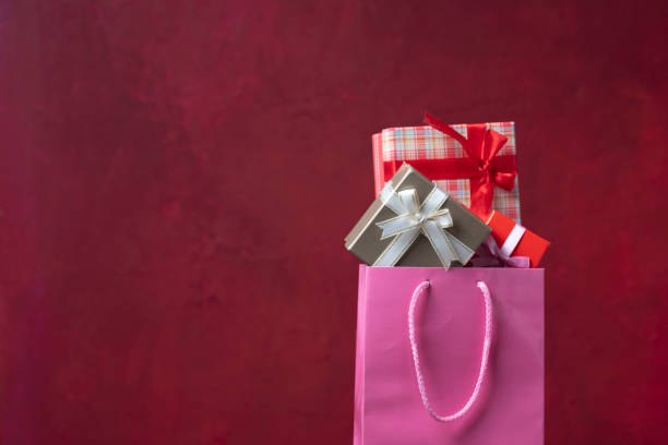 Photo of pink shopping bag full of gift boxes on red background. No people are seen in frame. Shot with a full frame mirrorless camera in studio.