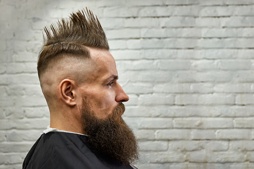 portrait of a man with a mohawk and beard in a barber chair against a brick wall. close up, brick background, copy space.