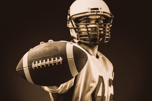 American football player holding the ball in his hands in front of the camera. Concept American football, motivation, black background.