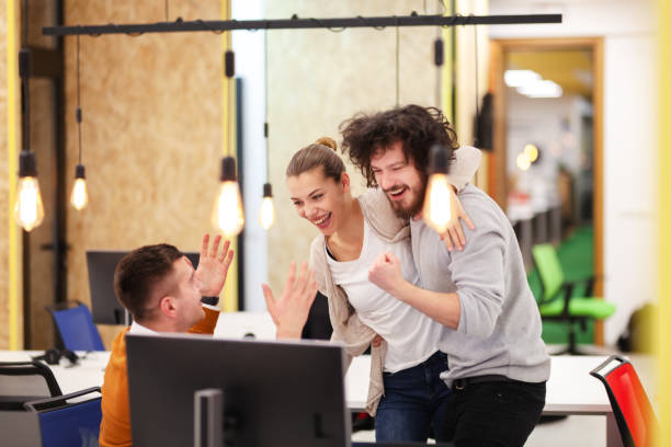 istock Three caucasian colleagues cheering for job well done in a modern office with decorative hanging lightbulbs 1352540116