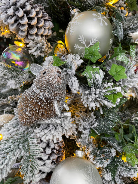 nahaufnahme von mausornament, mit glitzer verzierten silbernen kugeln, die am faden an künstlichen weihnachtsbaumzweigen hängen, mit künstlichem sprühschnee bedeckte fichtennadeln, verschwommener weißer lichterkettenhintergrund - flitter mouse stock-fotos und bilder