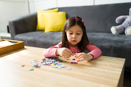 Young little girl playing alone in the living room and putting together a puzzle