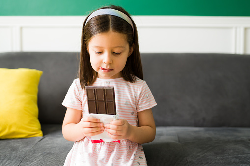 Sweet cravings. Adorable elementary girl receiving a treat and licking her lips while holding a big chocolate candy bar