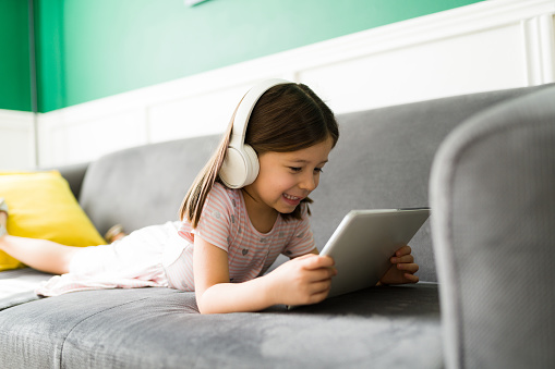 Excited elementary kid relaxing on the couch while watching online videos or movies on the tablet at home