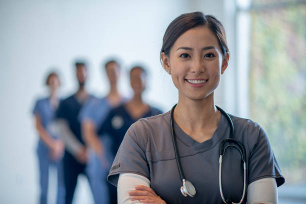 Medical Team Portrait A small group of diverse medical professionals stand in a hospital posing for a portrait.  They are each wearing scrubs and smiling, while the focus is on a female professional in front. nurse photos stock pictures, royalty-free photos & images