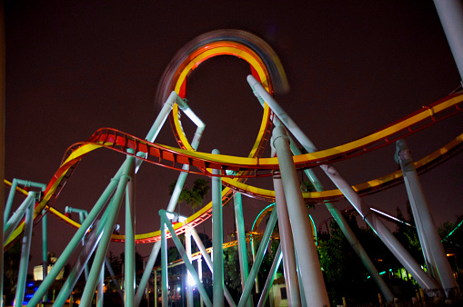 A low-angle, long-exposure wide shot of an inverted rollercoaster at night as the train goes over a loop
