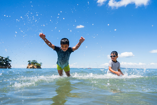 Mixed race kids jumping in the water at beach.