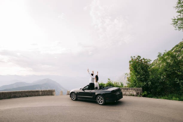 the bride and the groom are standing with their hands up in an open car in the picturesque mountains in montenegro - bride wedding freedom arms raised imagens e fotografias de stock