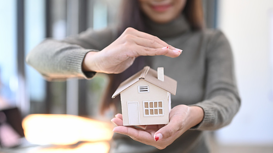 Smiling woman holding small house model. Real estate and property insurance concepts.