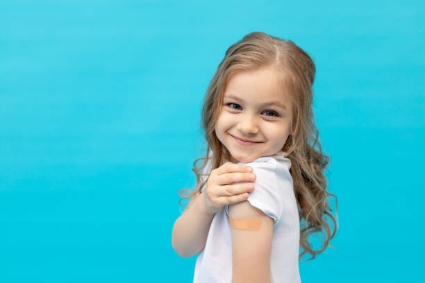 スタジオの青い背景に白いtシャツ、テキストのためのスペース、予防接種、健康と医学の概念でワクチン接種後、彼女の腕にパッチを持つ小さな女の子の子供 - little girls vaccination child caucasian ストックフォトと画像
